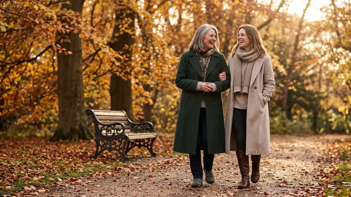 Older mother and adult daughter walking arm in arm through an English park in autumn