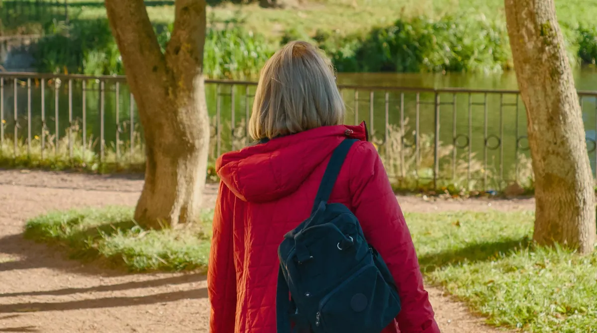 Woman in a red jacket walking along a park path, a simple daily habit that supports fat loss